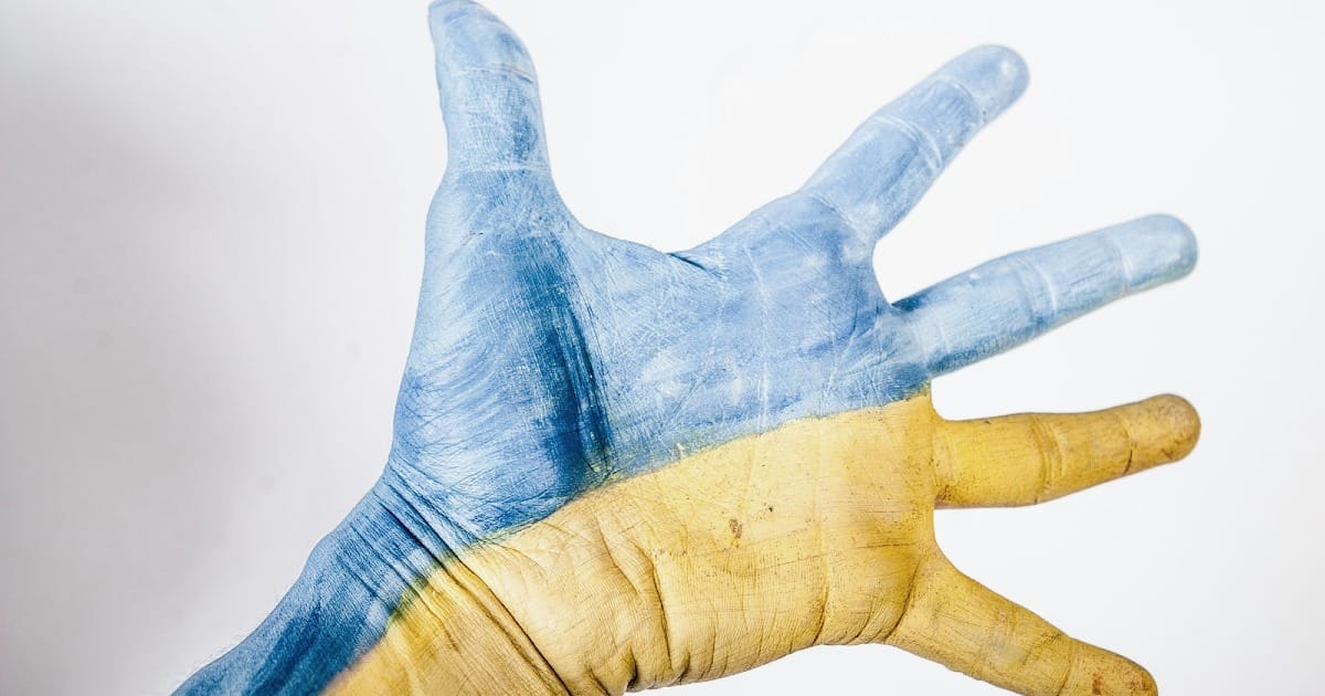 A Ukrainian hand painted in national colours reaches out for support